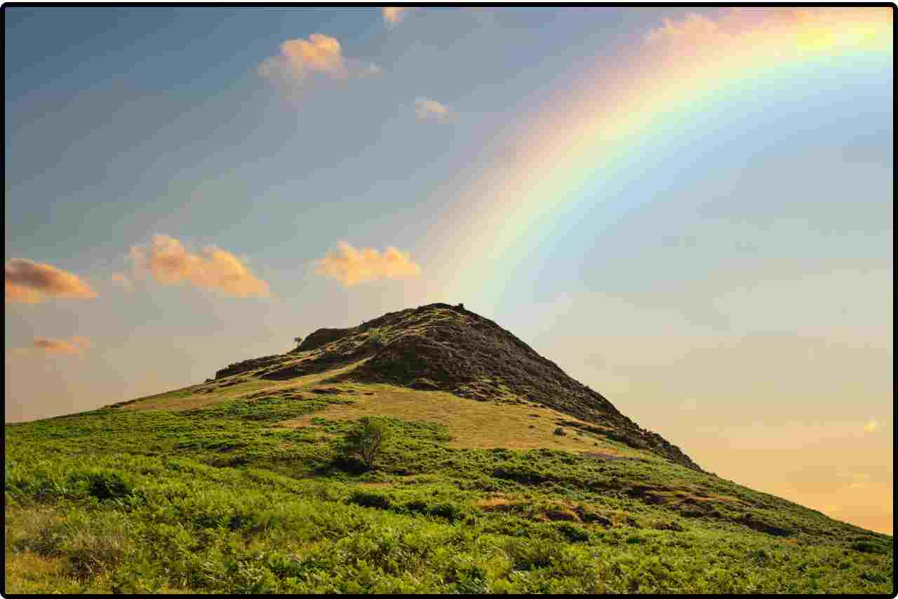 Close-up of a rainbow emerging from misty clouds above a serene mountain valley.